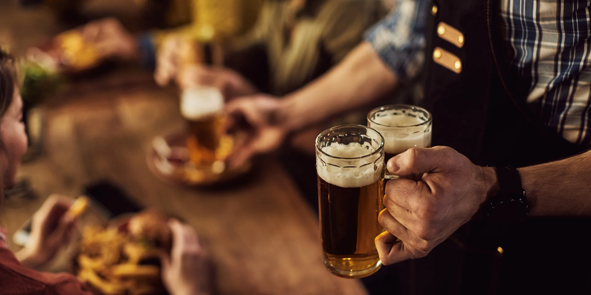 Close-up of waiter serving beer to customers in a pub.